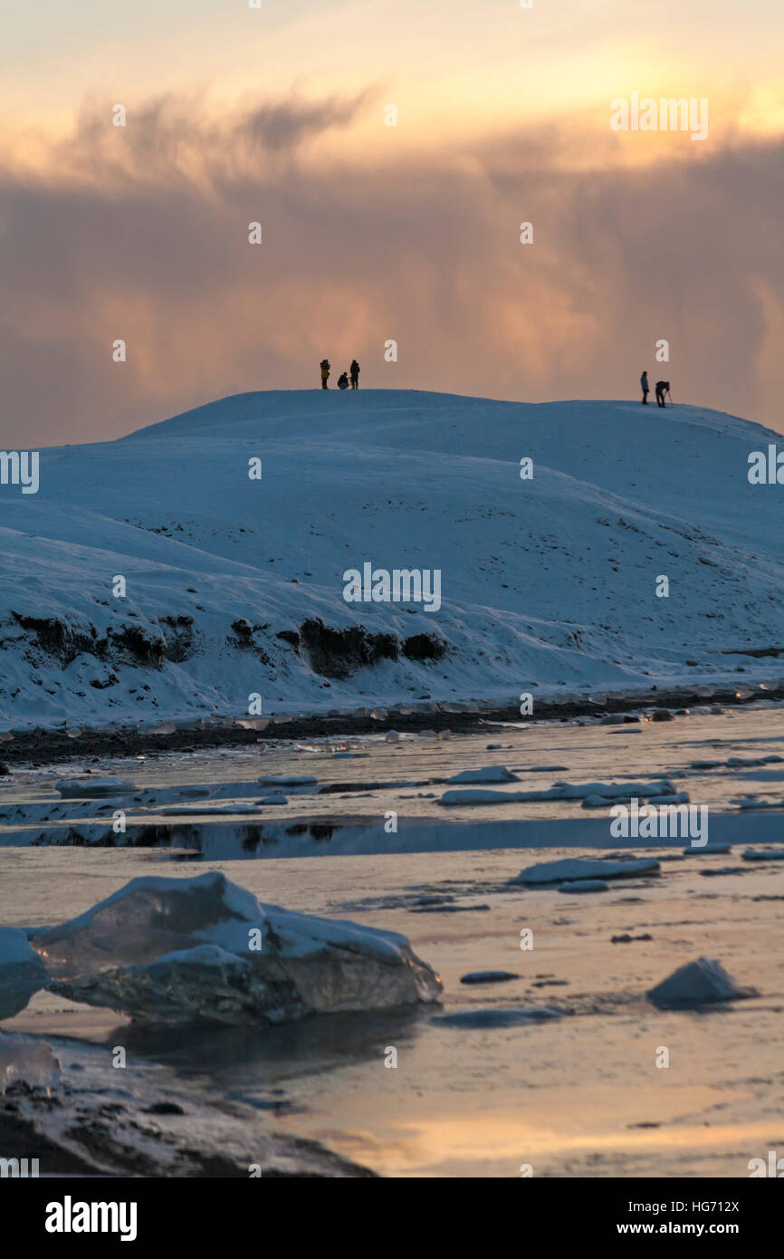 Les touristes prenant des photos sur montagne à Jokulsarlon Glacial Lagoon, sur le bord du Vatnajokull National Park, à l'aube, de l'Islande en Janvier Banque D'Images