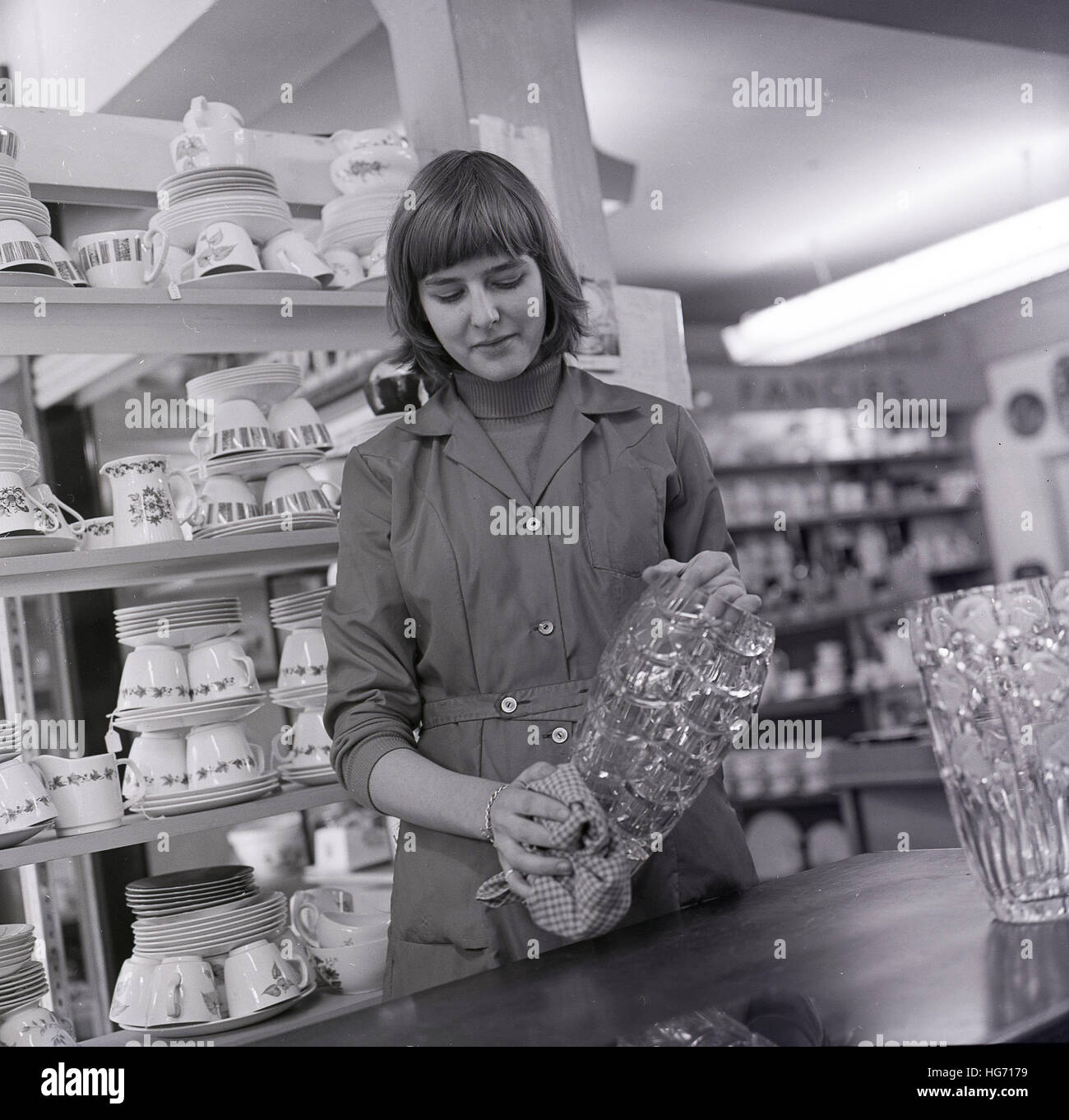 Années 1960, historiques, jeune femme shop assistant nettoie la verrerie vaisselle dans le ministère. Banque D'Images