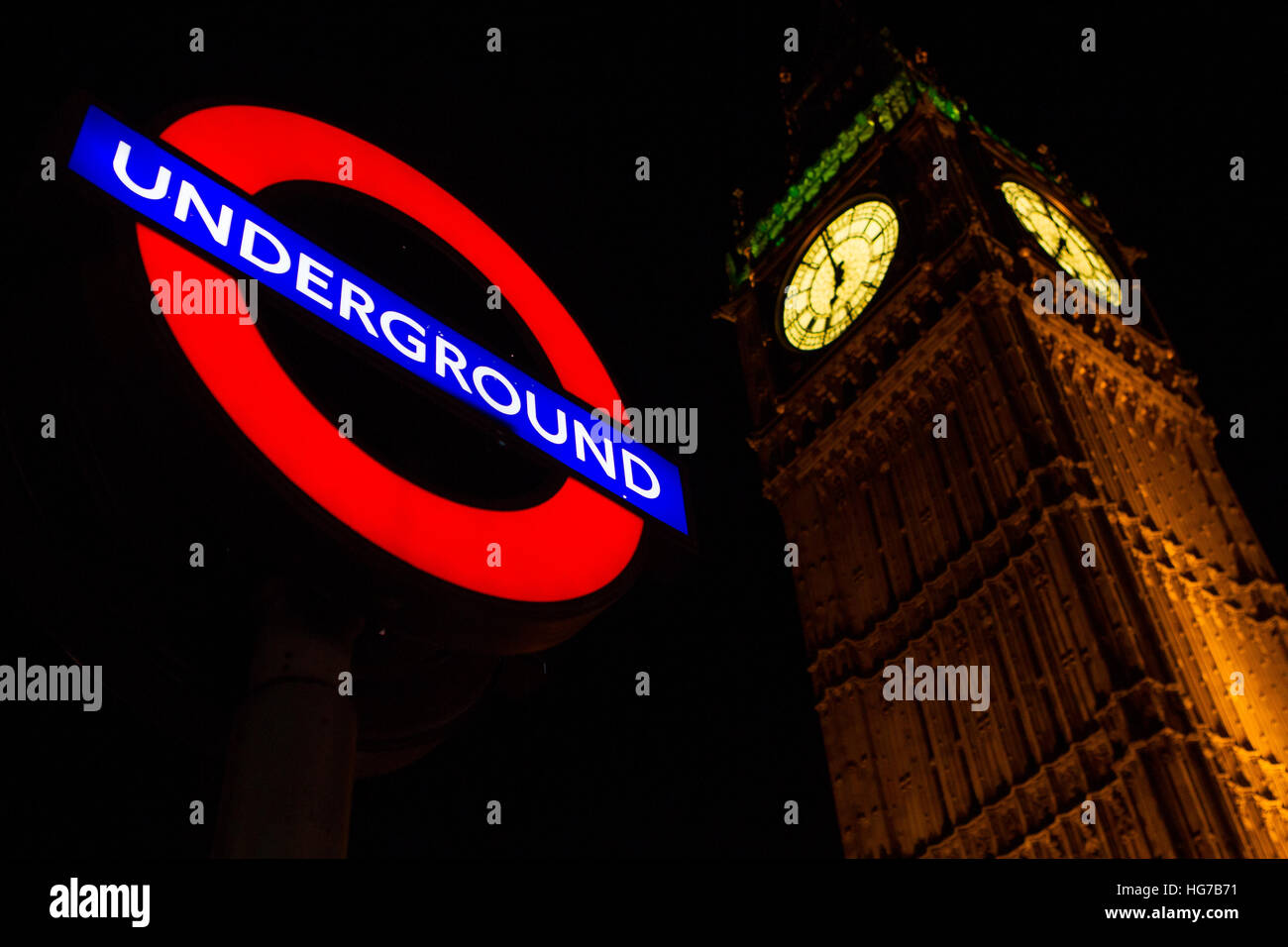 London Underground tube lumineux cocarde de signer dans l'obscurité la nuit à côté de Big Ben et le palais de Westminster, le Parlement Banque D'Images