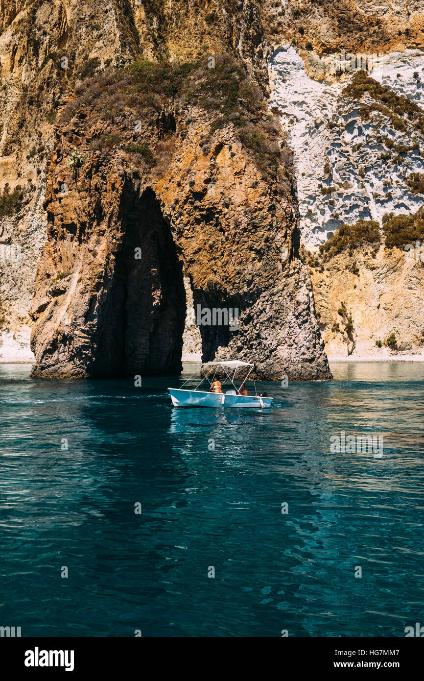 Un petit bateau naviguant sur le 'Arco Naturale', un passage rocheux naturel au large de la côte de l'île de Ponza, Italie. Banque D'Images