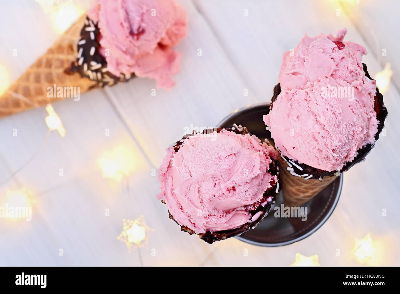 Vue de dessus de la crème glacée aux fraises rose en cônes alvéolés tourné sur un fond en bois rustique avec fairy lights et plus icecream. Faible profondeur extrême Banque D'Images