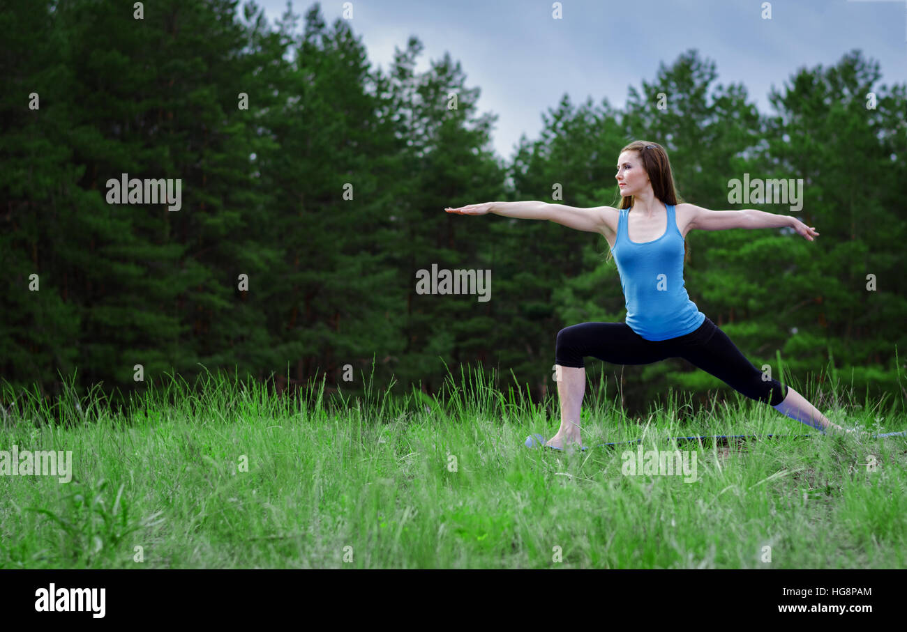 Jeune fille pratiquant le yoga dans la nature dans les bois sur un fond d'arbres et l'herbe verte. Banque D'Images