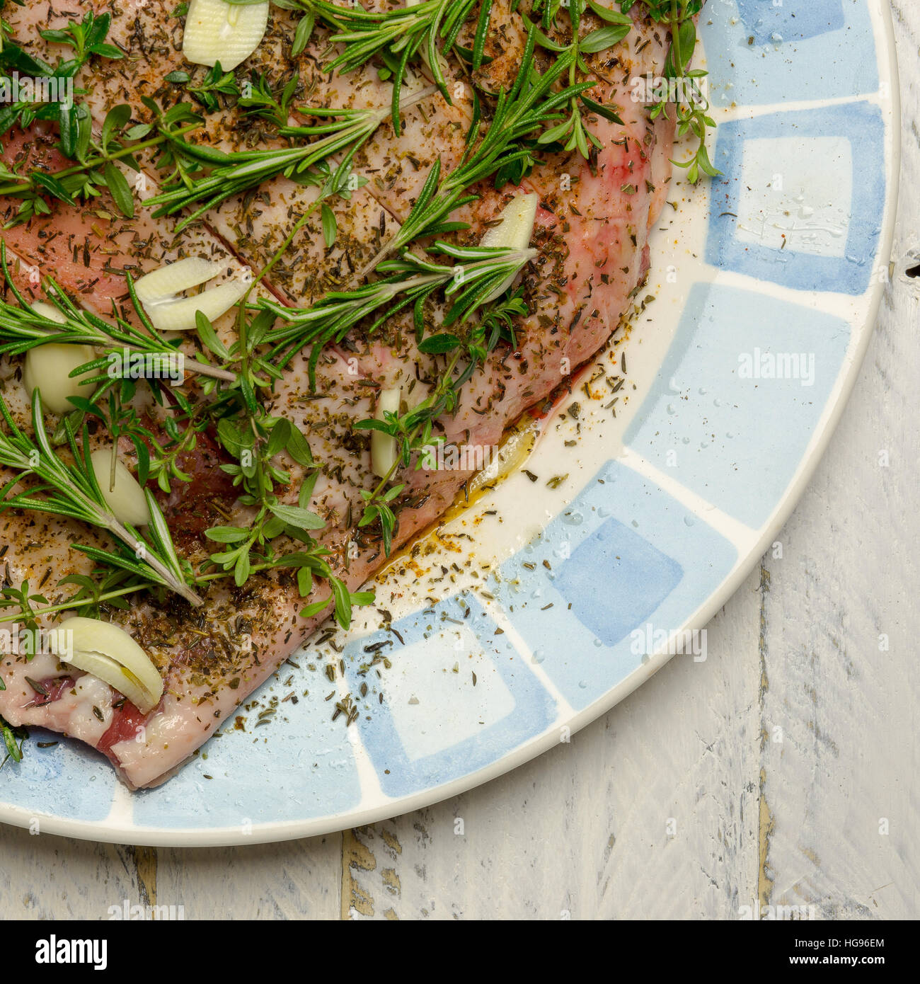 L'épaule de matières premières de viande d'agneau avec la marinade d'huile d'olive, ail, thym, romarin sur plaque avec ornement bleu Banque D'Images