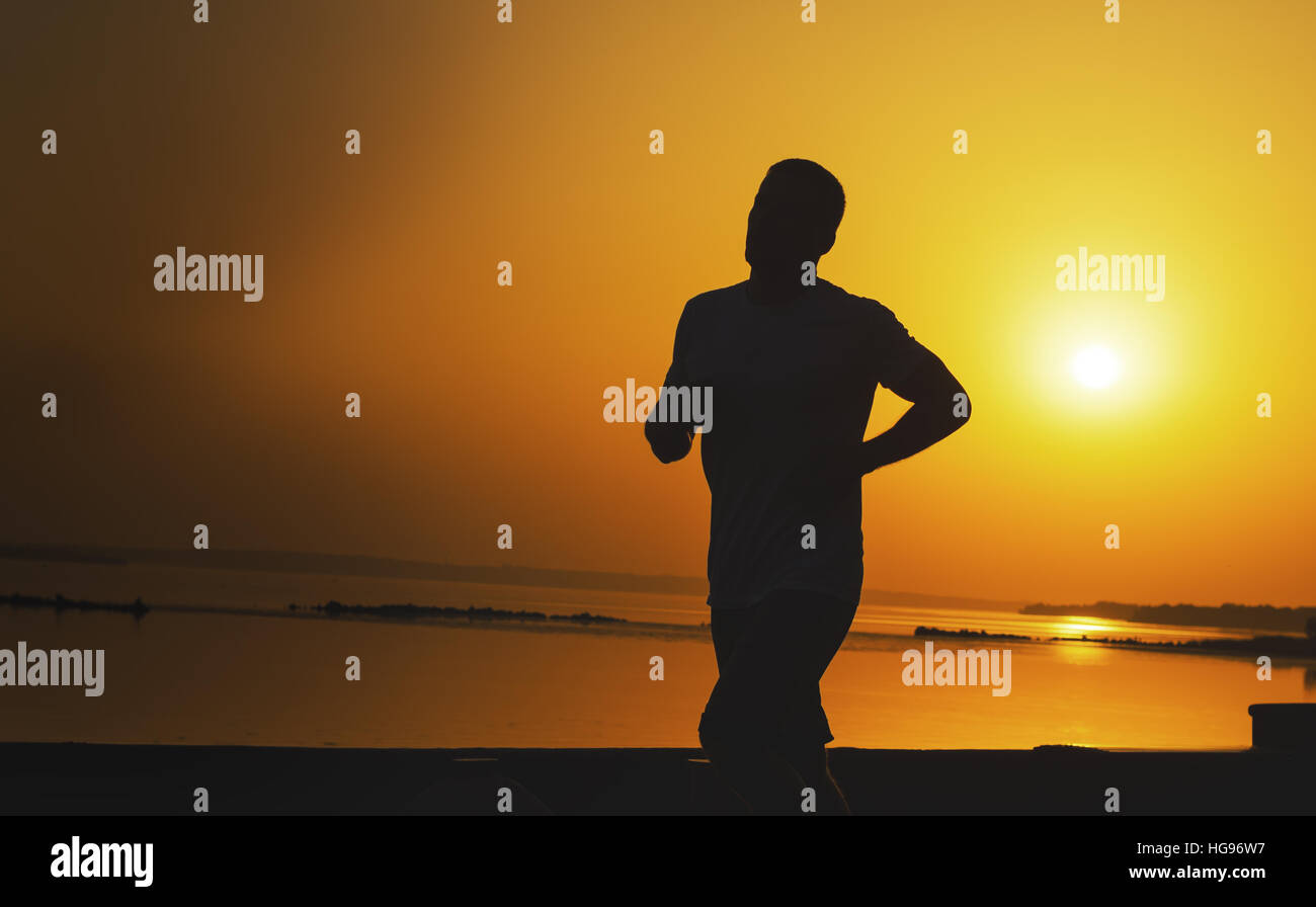 Silhouette d'homme qui court à l'extérieur, sur un fond de coucher du soleil orange. Banque D'Images