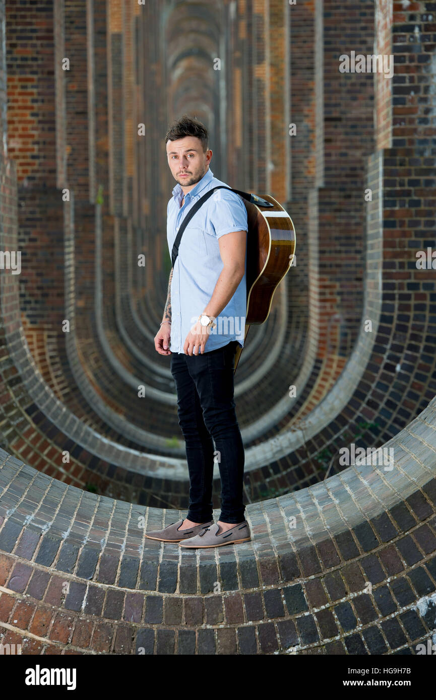 Chanteur, auteur-compositeur Jamie Mathias pose avec sa guitare pour un tournage à l'Ouse valley viaduc, Sussex, UK. Banque D'Images