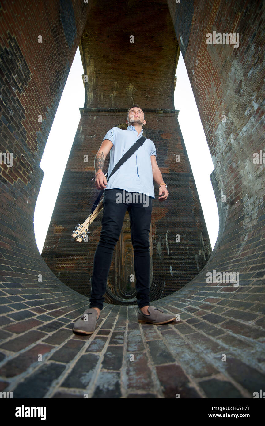 Chanteur, auteur-compositeur Jamie Mathias pose avec sa guitare pour un tournage à l'Ouse valley viaduc, Sussex, UK. Banque D'Images