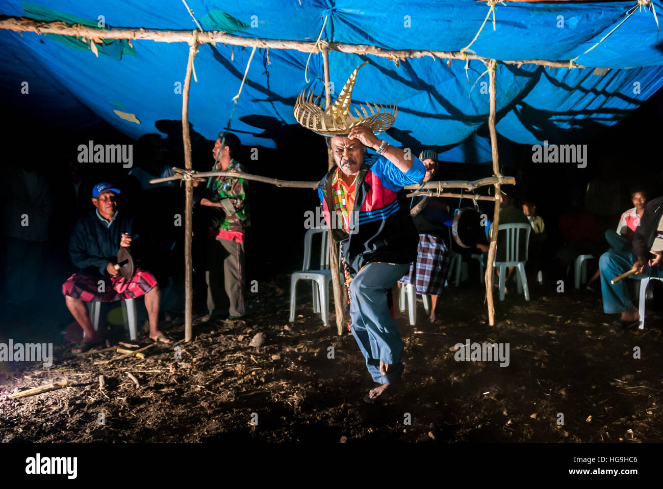 Un aîné portant une danse traditionnelle en tenue de chambre, dans un fond d'hommes jouant des instruments percussifs à Rote Island, à Nusa Tenggara est, Indonésie. Banque D'Images