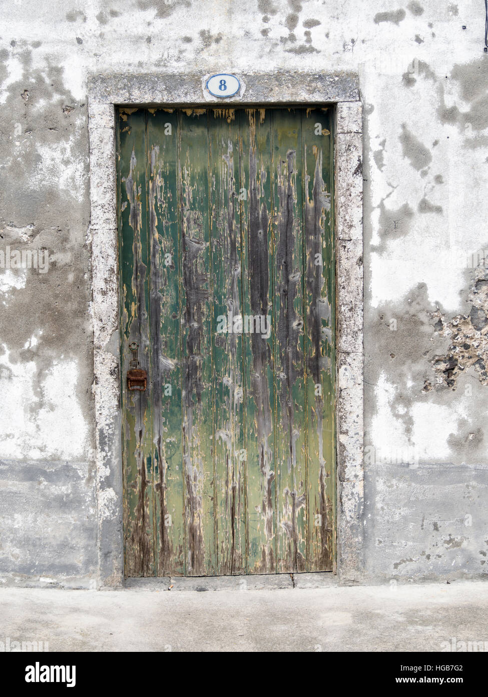 Vieille porte au numéro 8. L'écaillage de la peinture et une poignée de rouille marquer les années sur cette vieille porte de planches situé dans un mur en ruine. Banque D'Images