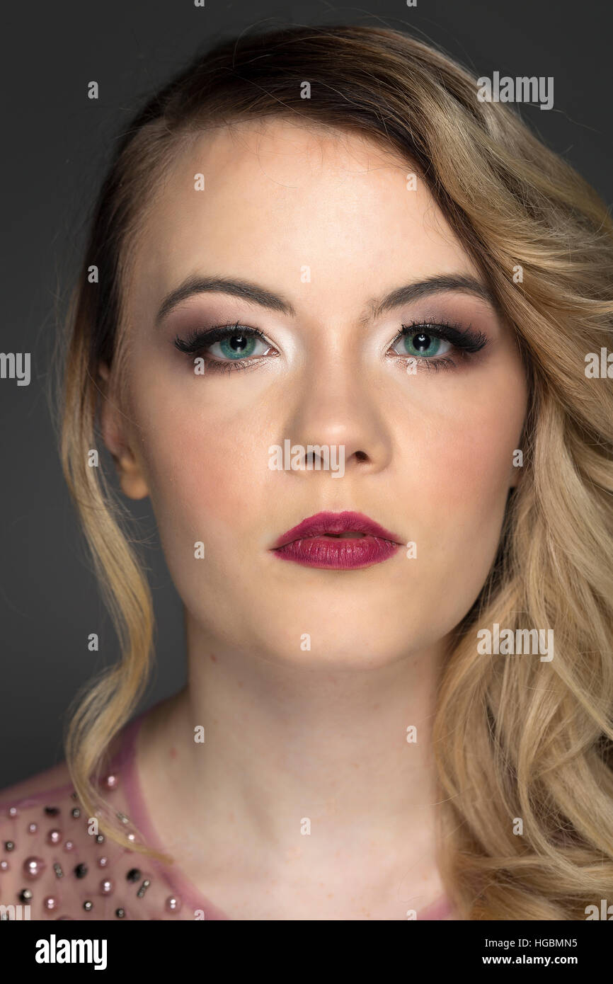 Portrait de modèle avec boucles blonde, maquillage naturel et profond  lèvres berry rose, portant des bijoux haut fond gris Photo Stock - Alamy