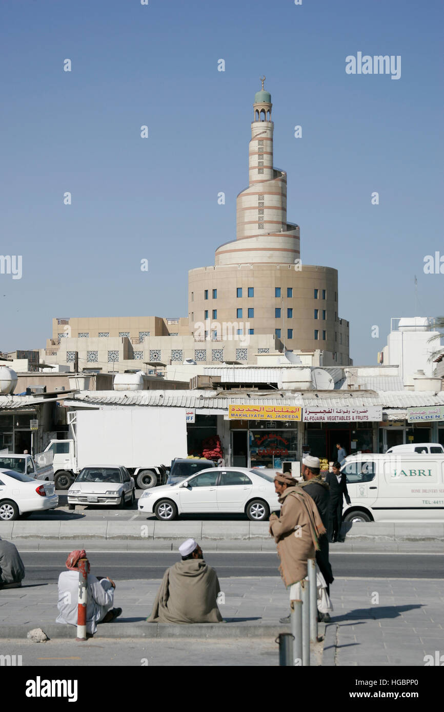 Qatar, Doha, les travailleurs de la construction assis sur la chaussée dans la vieille partie de la ville, dans l'arrière-plan la grande tour du FANAR Banque D'Images