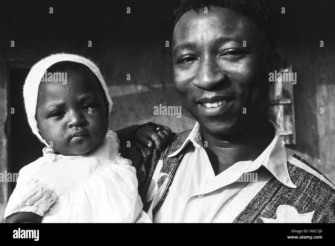 Un père de Jaiama Nimi Koro, Sierra Leone, tenant fièrement sa petite fille à l'extérieur de leur maison en 1963. Banque D'Images