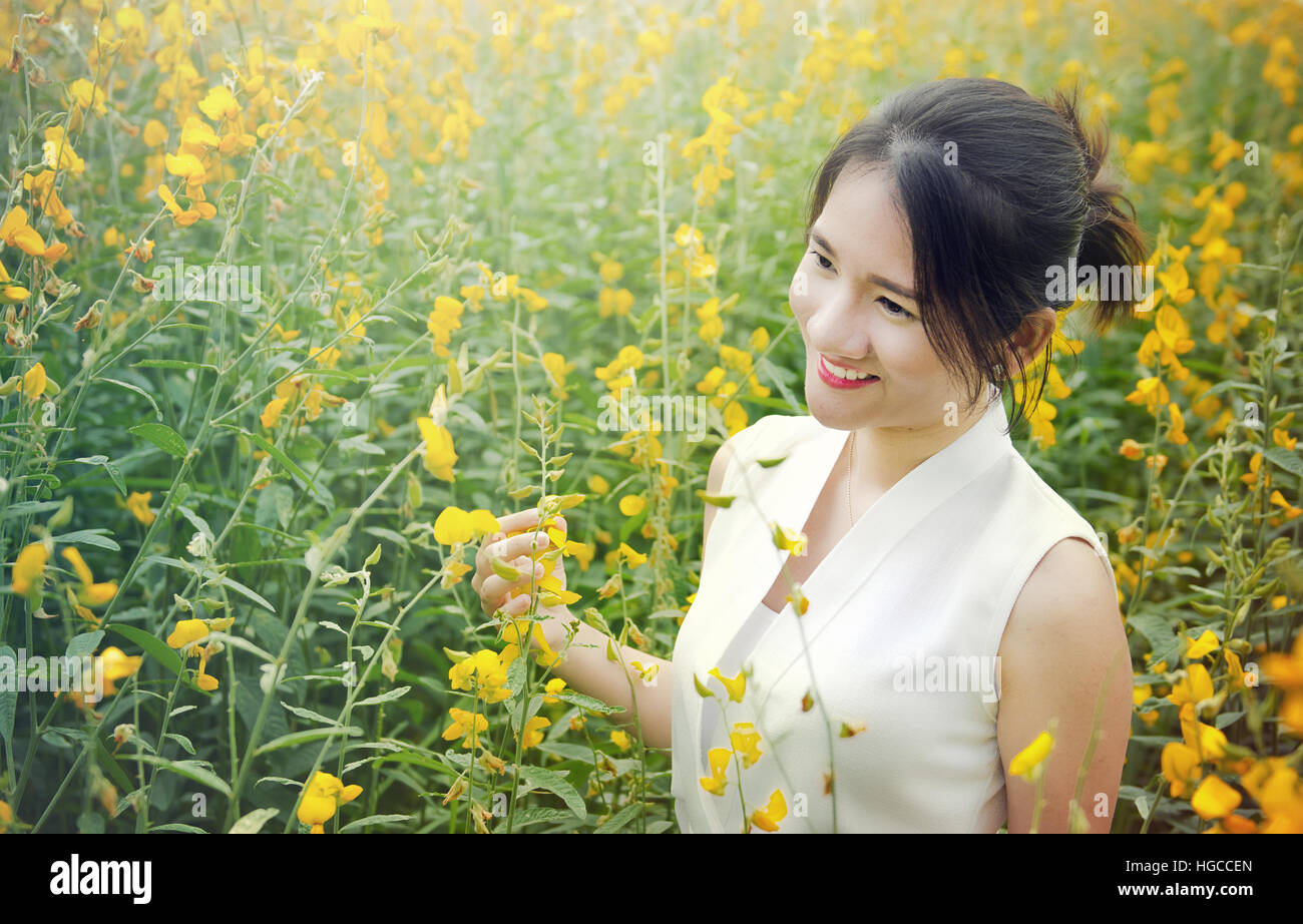 Photo Portrait de jeune fille thaïlandaise asiatique avec smiley face et lèvre rouge dans le jardin avec la lumière du matin et jaune (crotalaria juncea) sunhemp ba fleurs Banque D'Images