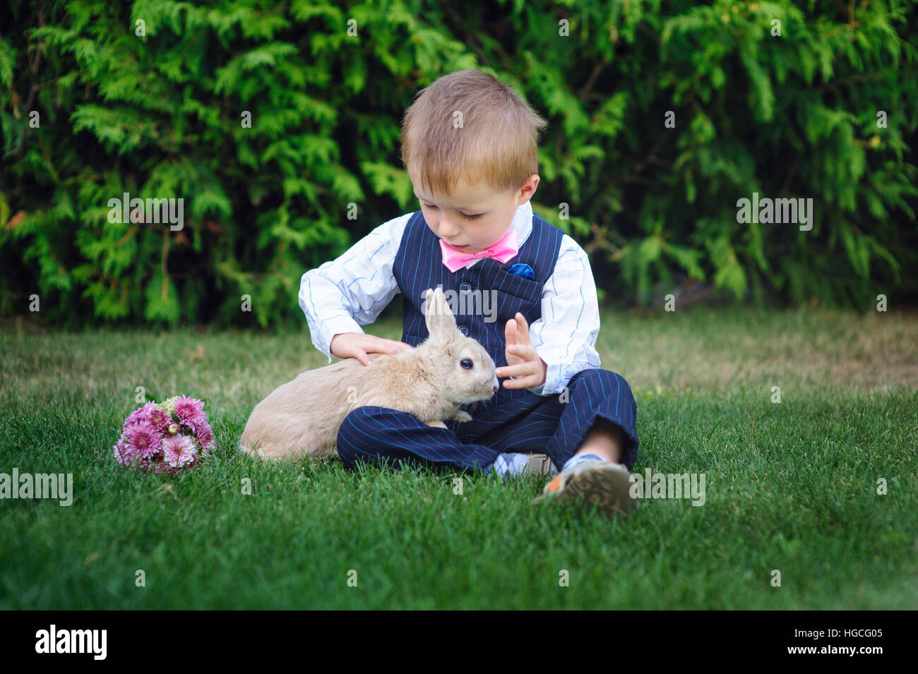 Petit garçon assis sur l'herbe avec lapin dans le parc d'été Banque D'Images