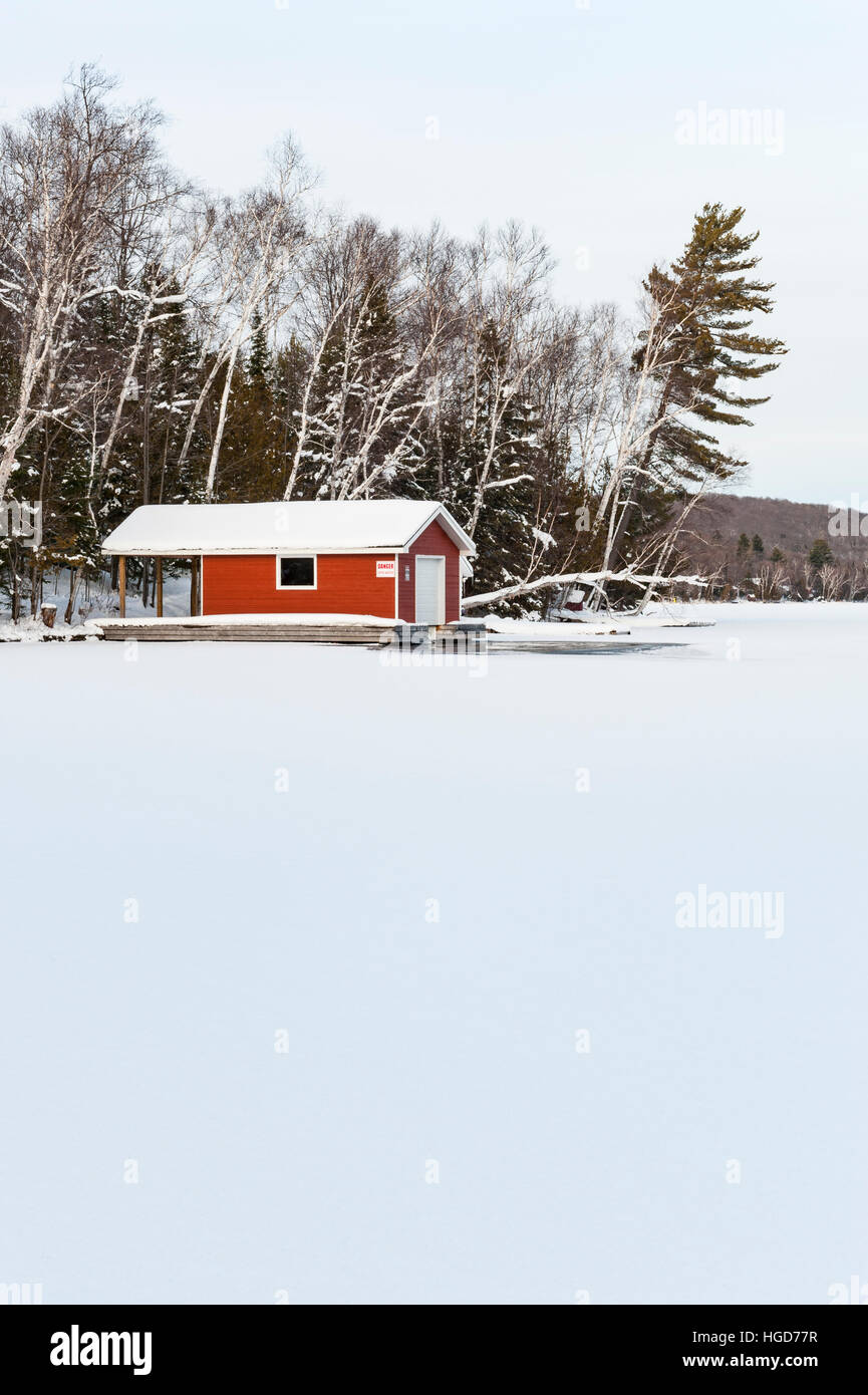 Paysage de neige canadien, hangar à bateaux rouge dans un lac gelé en hiver près de Huntsville, Ontario, ON, Canada. Banque D'Images