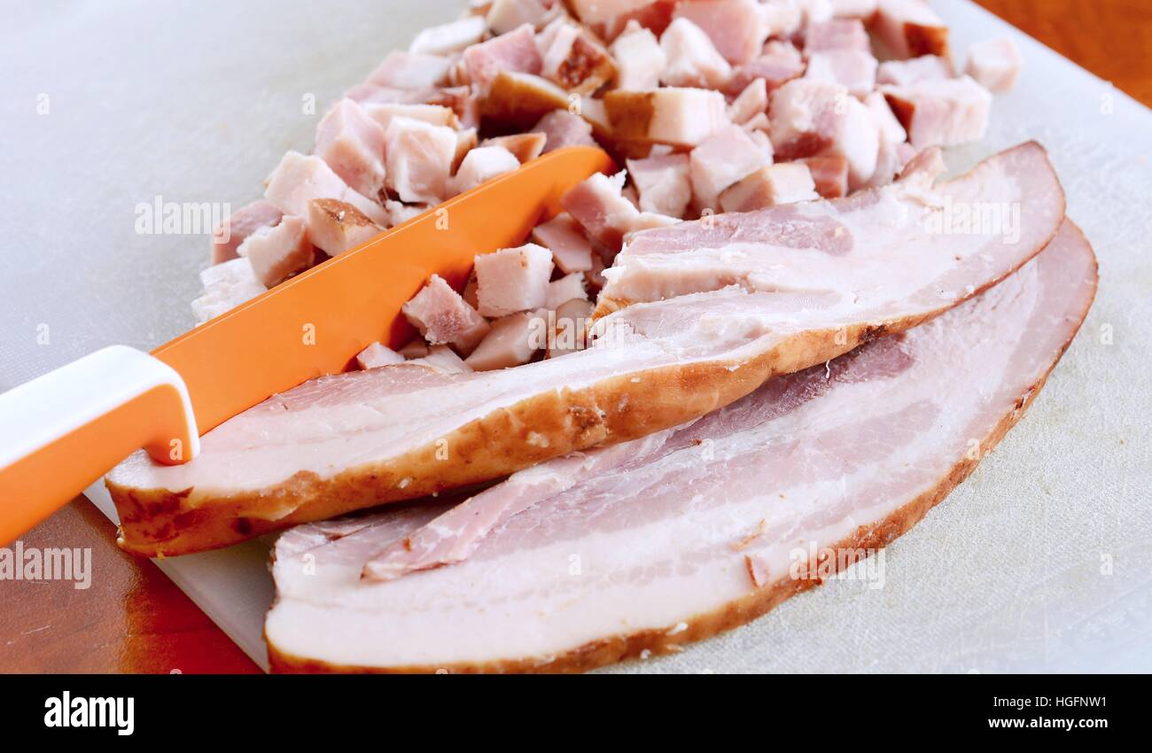 Libre de tranches de bacon et des cubes et orange couteau sur une planche à découper. Banque D'Images