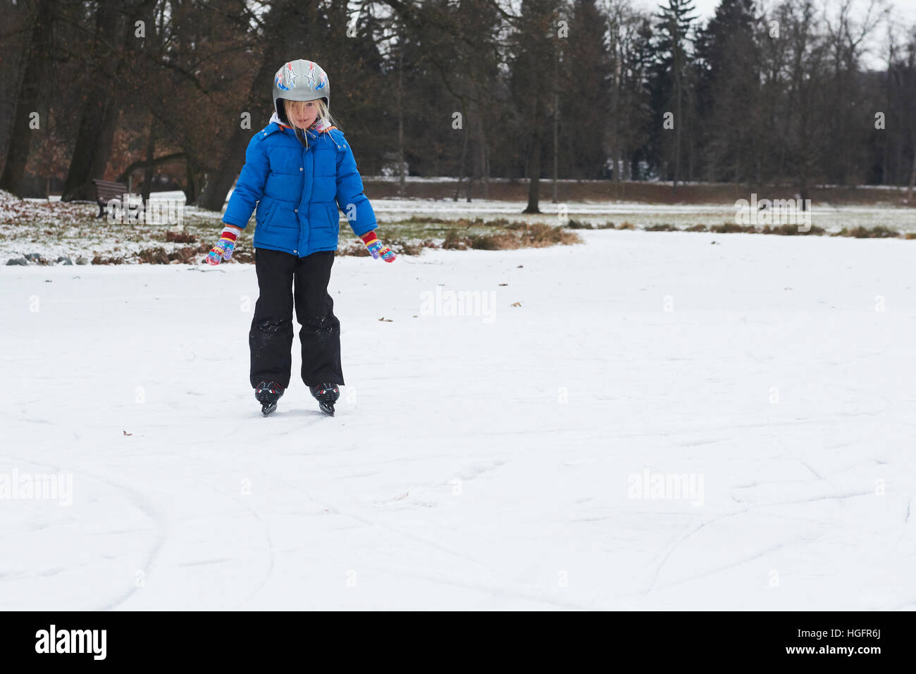 Adorable petite fille enfant patinage sur glace en hiver sous la neige à l'extérieur dans le parc sur étang gelé. Le port de casque de sécurité Banque D'Images