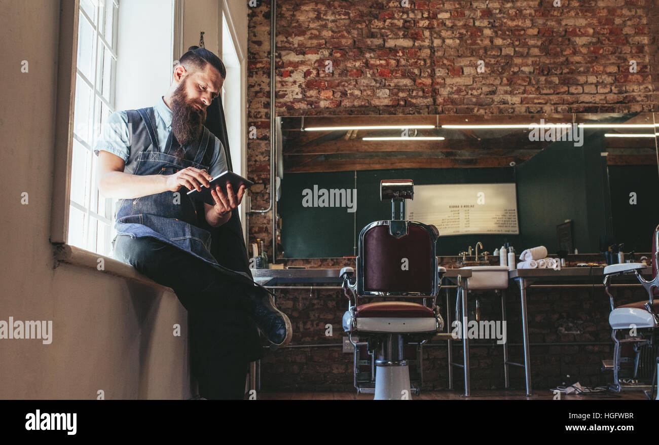 Hairstylist using digital tablet à son magasin. Coiffure assis à un coiffeur travaillant sur tablette numérique. Banque D'Images