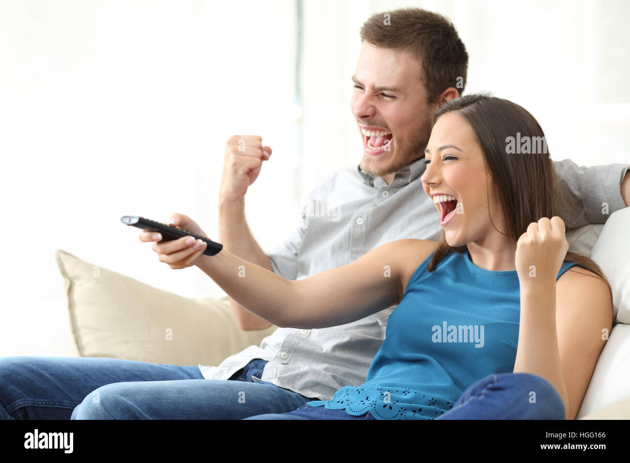 Heureux couple watching tv ensemble assis sur un canapé dans la salle de séjour à la maison Banque D'Images