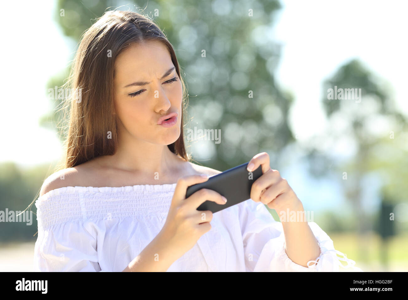 Surpris fille jouer à des jeux en ligne avec un téléphone intelligent dans un parc Banque D'Images