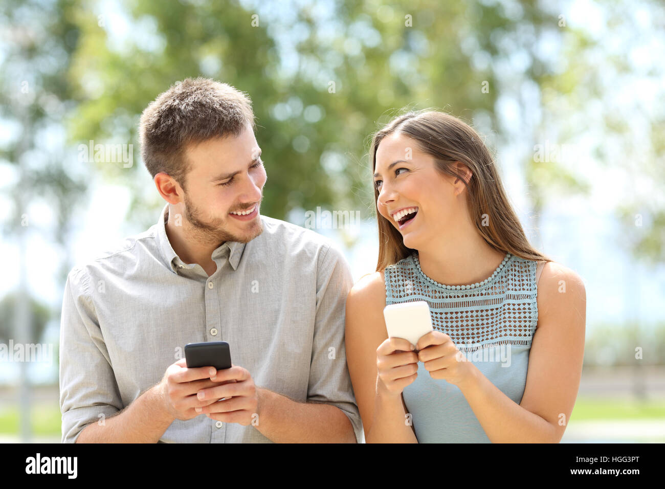 Vue de face d'un couple ou entre amis et plaisanter avec les téléphones intelligents à la ligne à l'extérieur dans un parc Banque D'Images