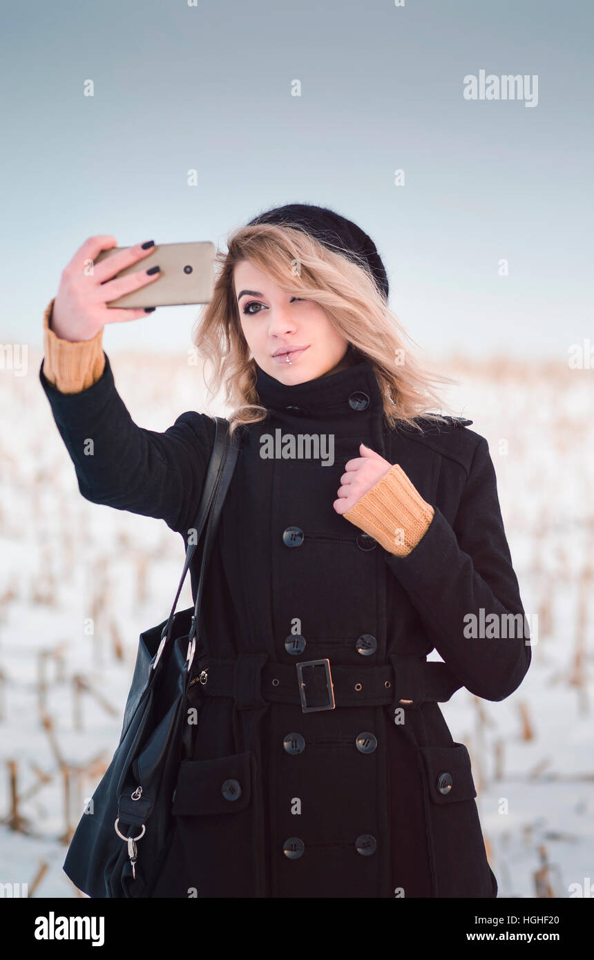 Jeune fille blonde d'autres dans des vêtements noirs en tenant dans les selfies champ neigeux Banque D'Images