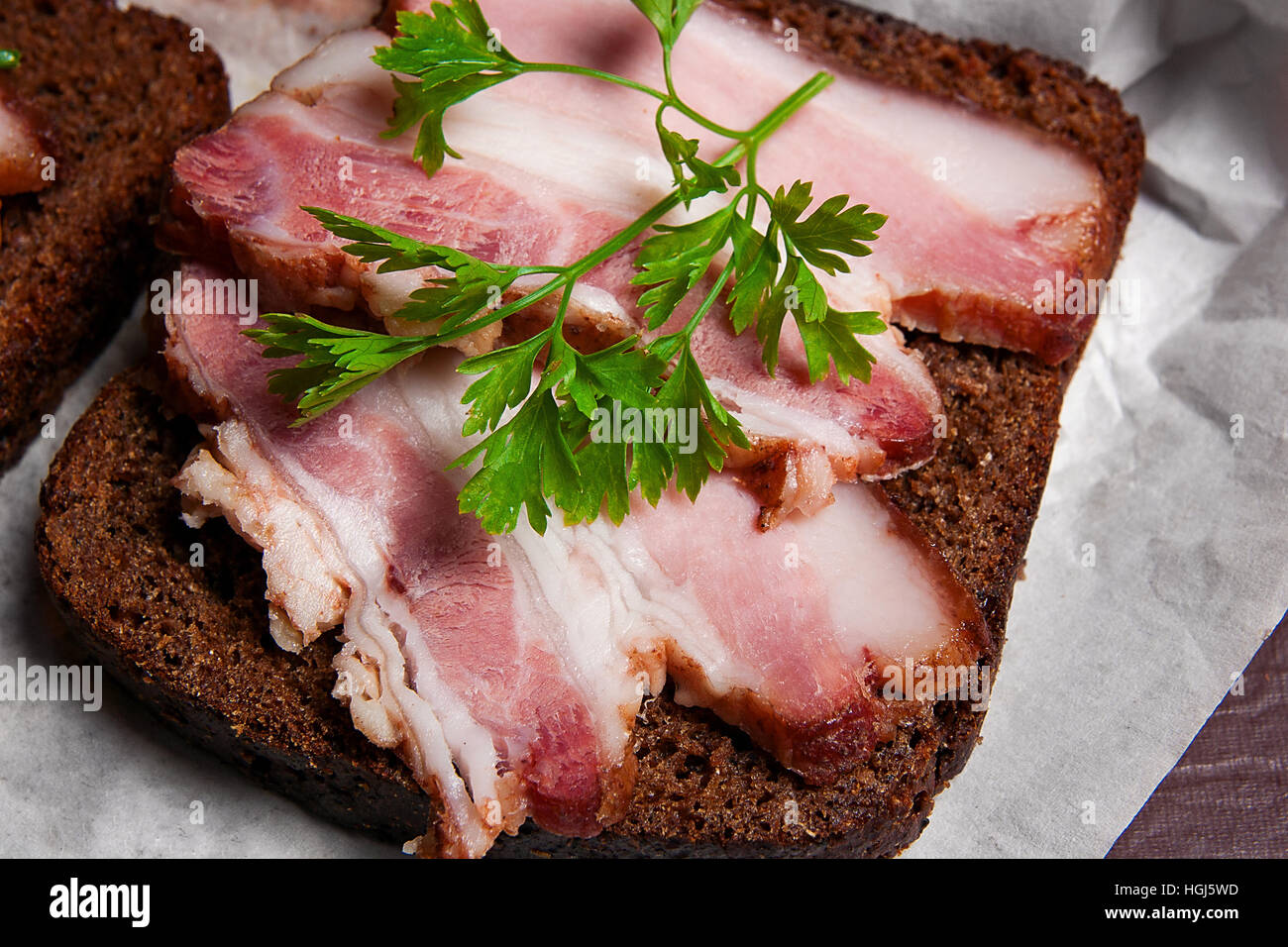 Vue rapprochée des tranches de lard fumé sur le morceau de pain de seigle avec des herbes - style rustique sur brown vintage. Banque D'Images