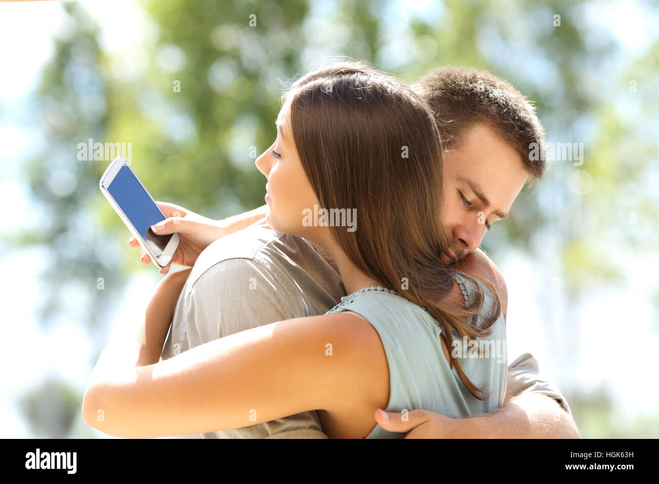 Copine triche texting sur le téléphone et s'étreindre son petit ami innocent Banque D'Images