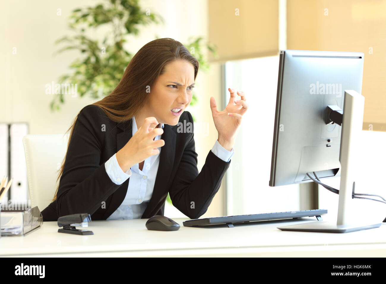 Furious businesswoman wearing suit en utilisant un ordinateur de bureau à la ligne à côté d'une fenêtre à l'office de tourisme Banque D'Images