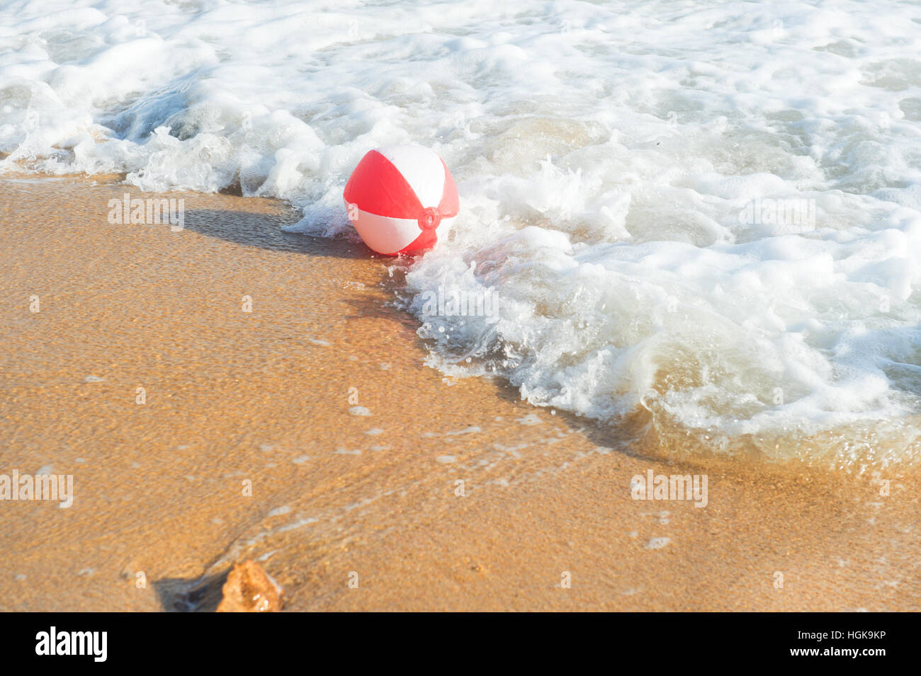 Ballon de plage rouge et blanc jouant avec les vagues et la mer à la plage Banque D'Images