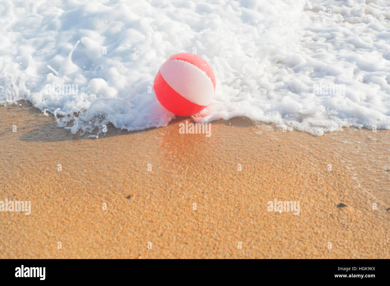Ballon de plage rouge et blanc jouant avec les vagues et la mer à la plage Banque D'Images