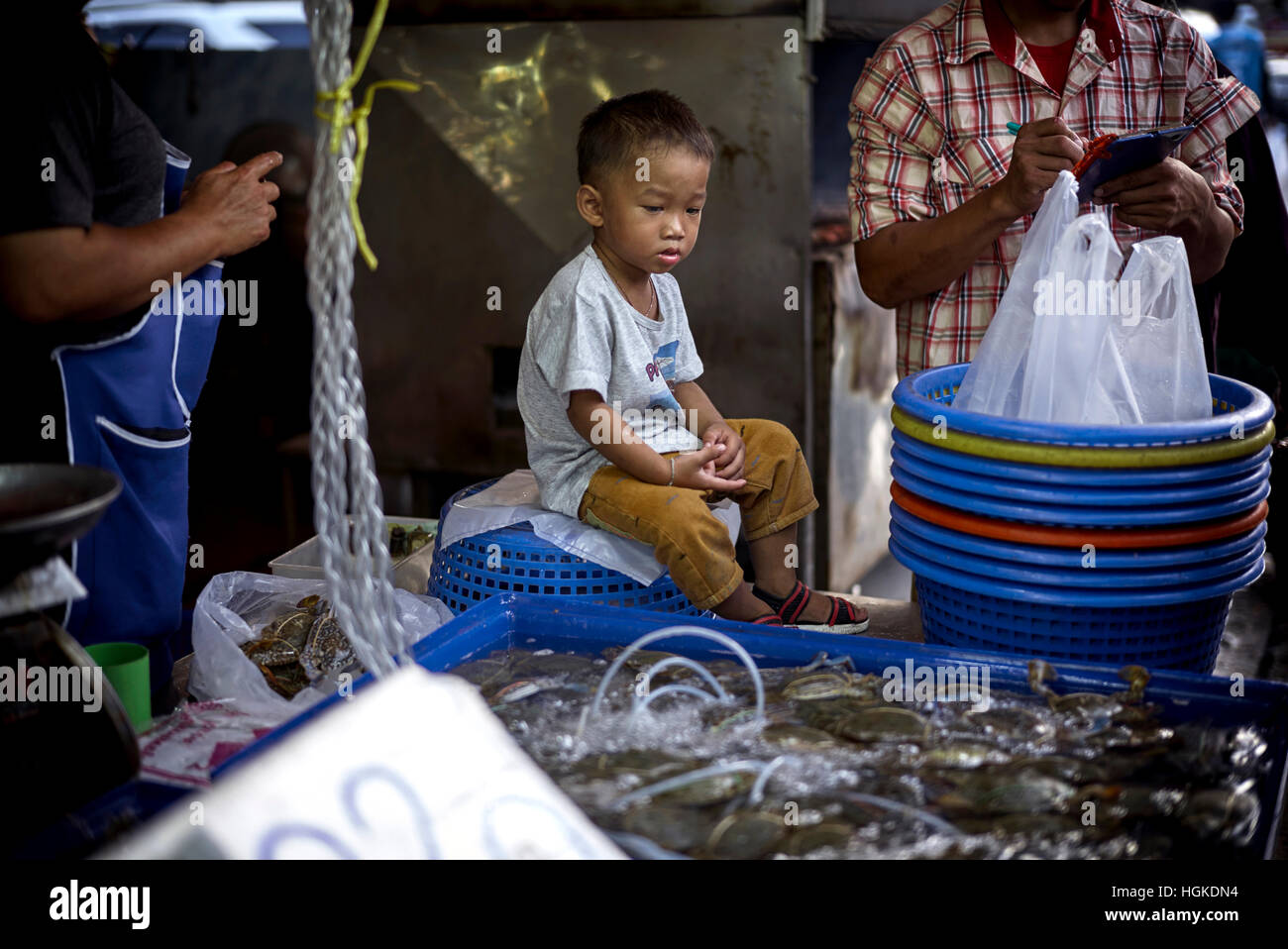 Enfant s'ennuie. Garçon s'assit au marché aux poissons frais de sa famille et s'ennuiait clairement et ne se contentait pas de sa situation. Thaïlande S. E. Asie Banque D'Images