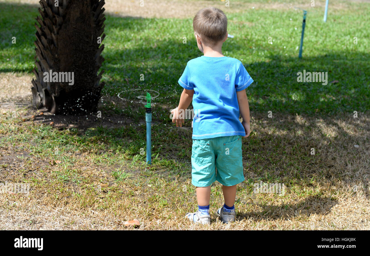 Jeune garçon jouant avec l'eau d'un arrosoir dans le jardin Banque D'Images
