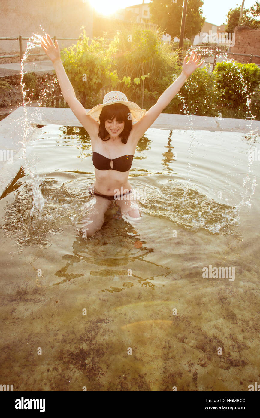 Jeune femme portant un bikini noir jouant avec de l'eau dans une piscine naturelle à l'été Banque D'Images