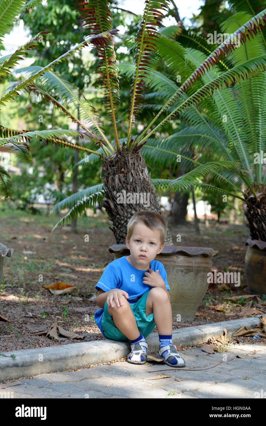 Joli garçon assis dans un jardin tropical Banque D'Images