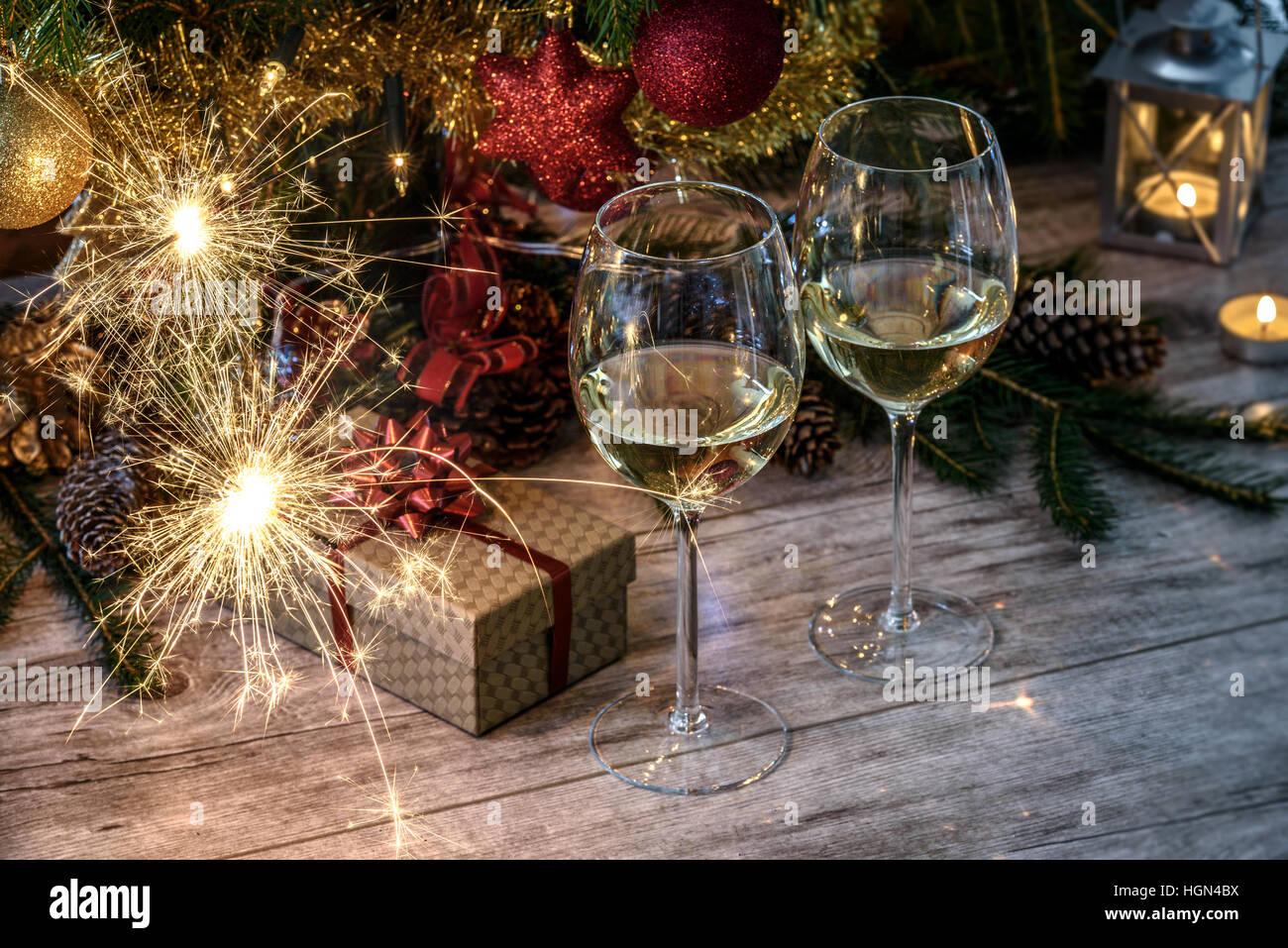 Cierges à deux wineglas avec vin blanc sur une table en bois à l'arrière-plan d'arbre de Noël, bougies et cadeaux Banque D'Images