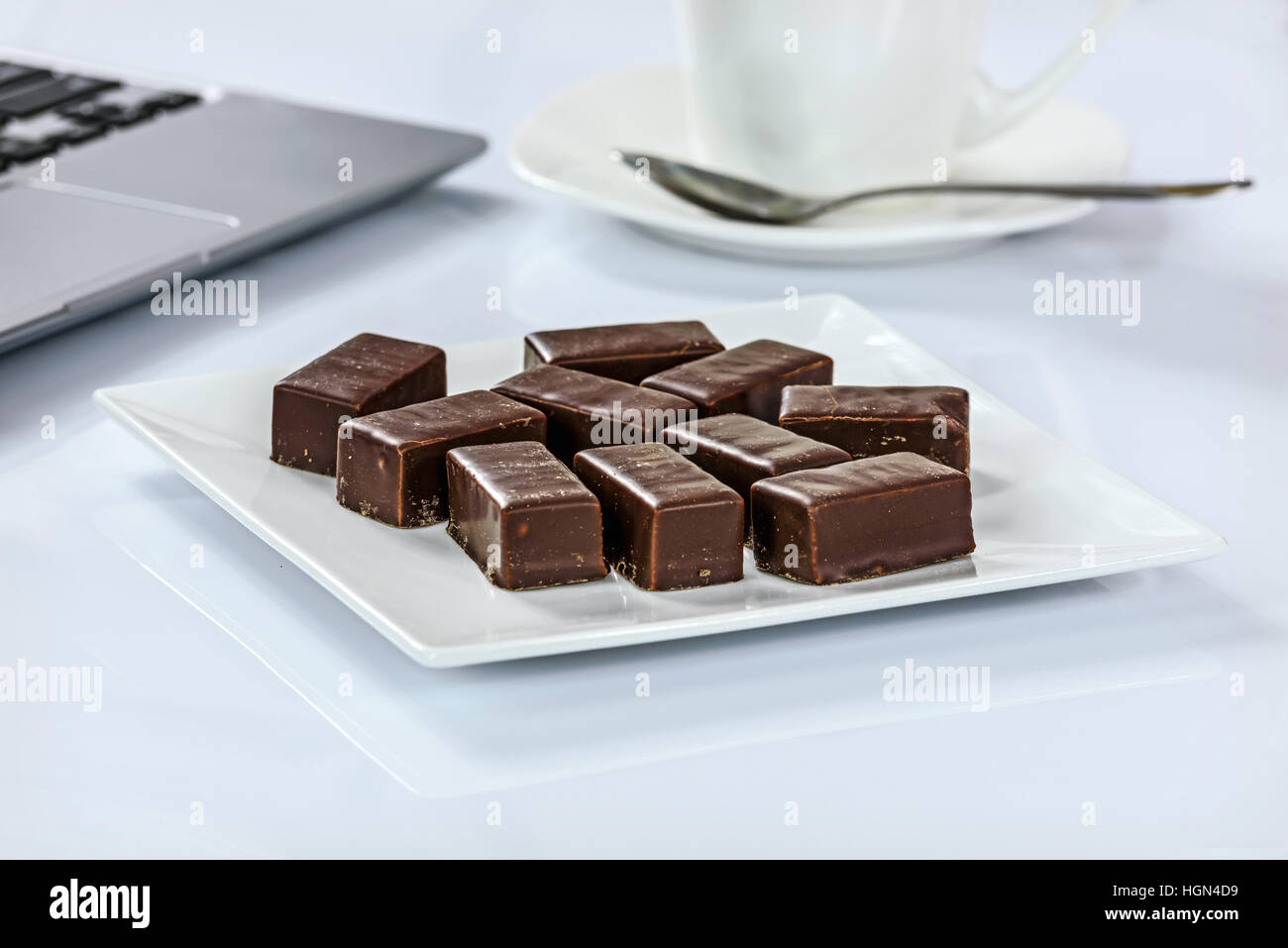 Les chocolats sur une plaque à côté d'une tasse de café et d'un ordinateur portatif dans le bureau Banque D'Images