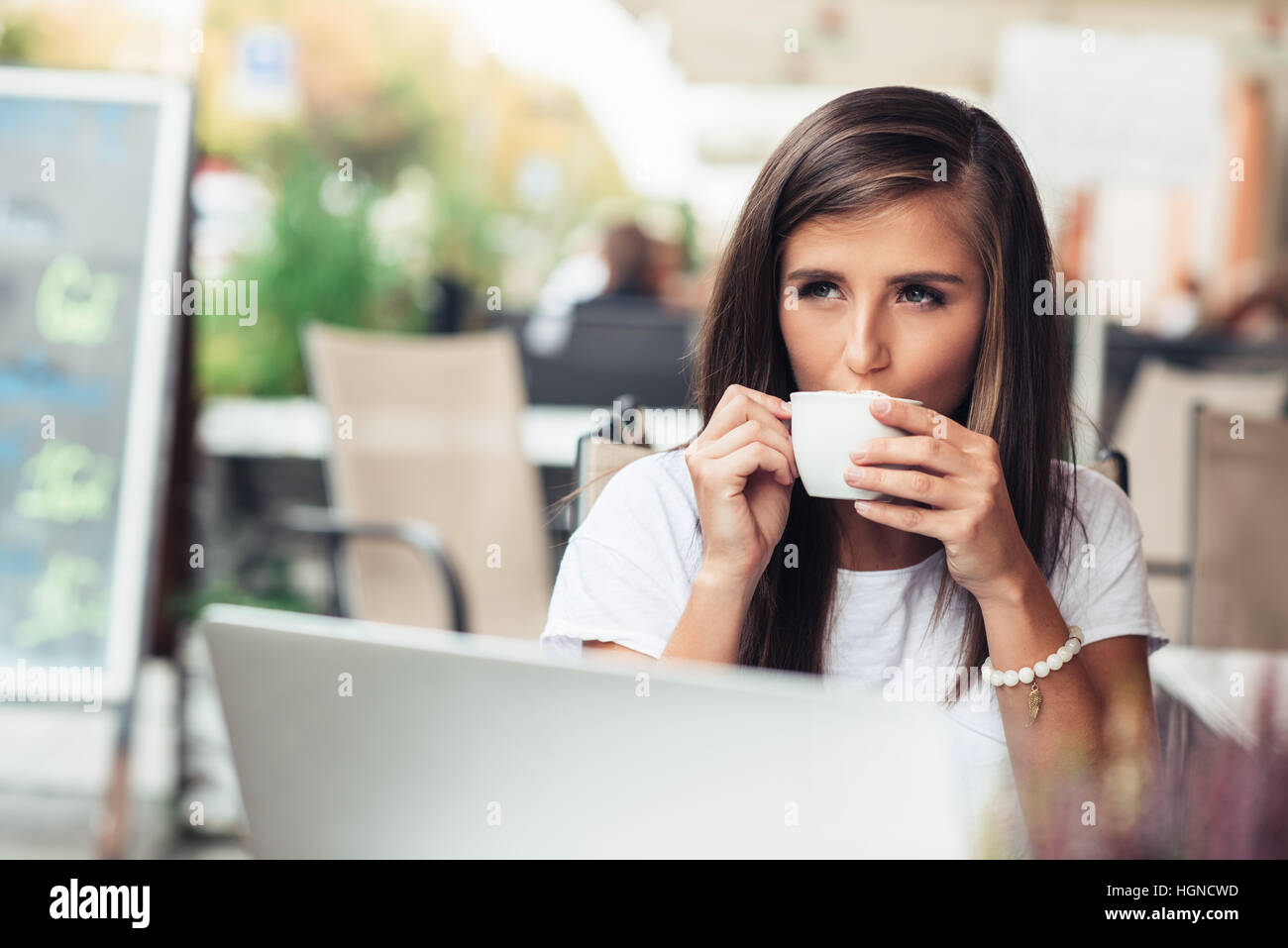 Attractive young woman drinking coffee at a sidewalk cafe Banque D'Images
