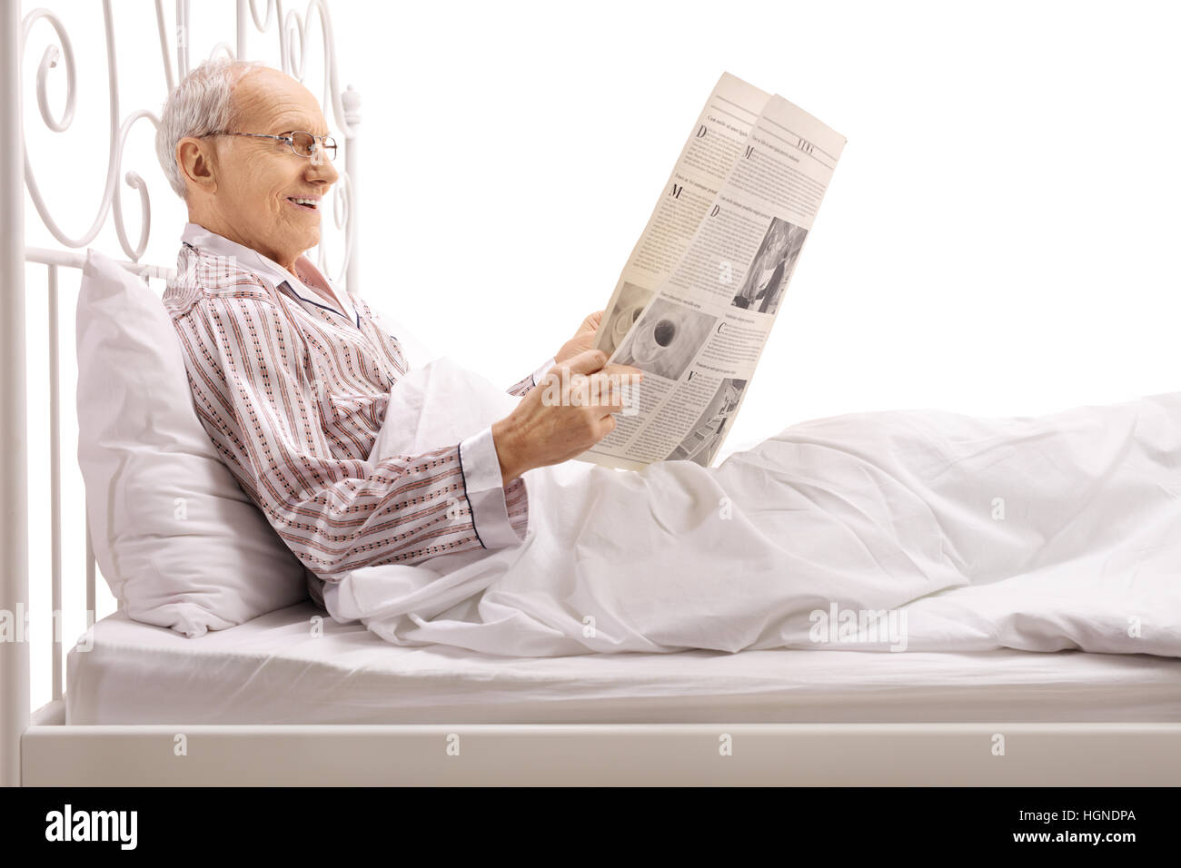 Homme mûr au lit et lire un journal isolé sur fond blanc Banque D'Images