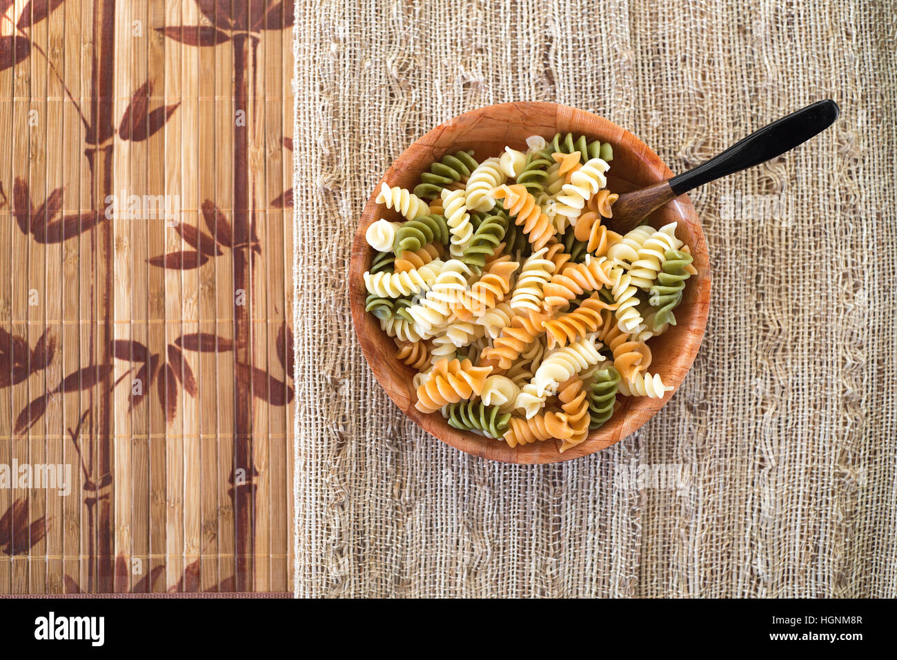 Un bol en bois avec les pâtes rotini multicolores sur une toile table cloth. Banque D'Images