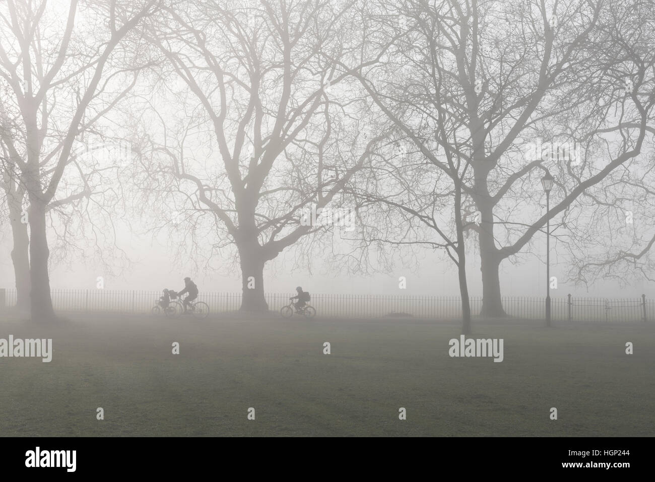 Une mère et 2 enfants à vélo à l'école le matin le brouillard. Banque D'Images