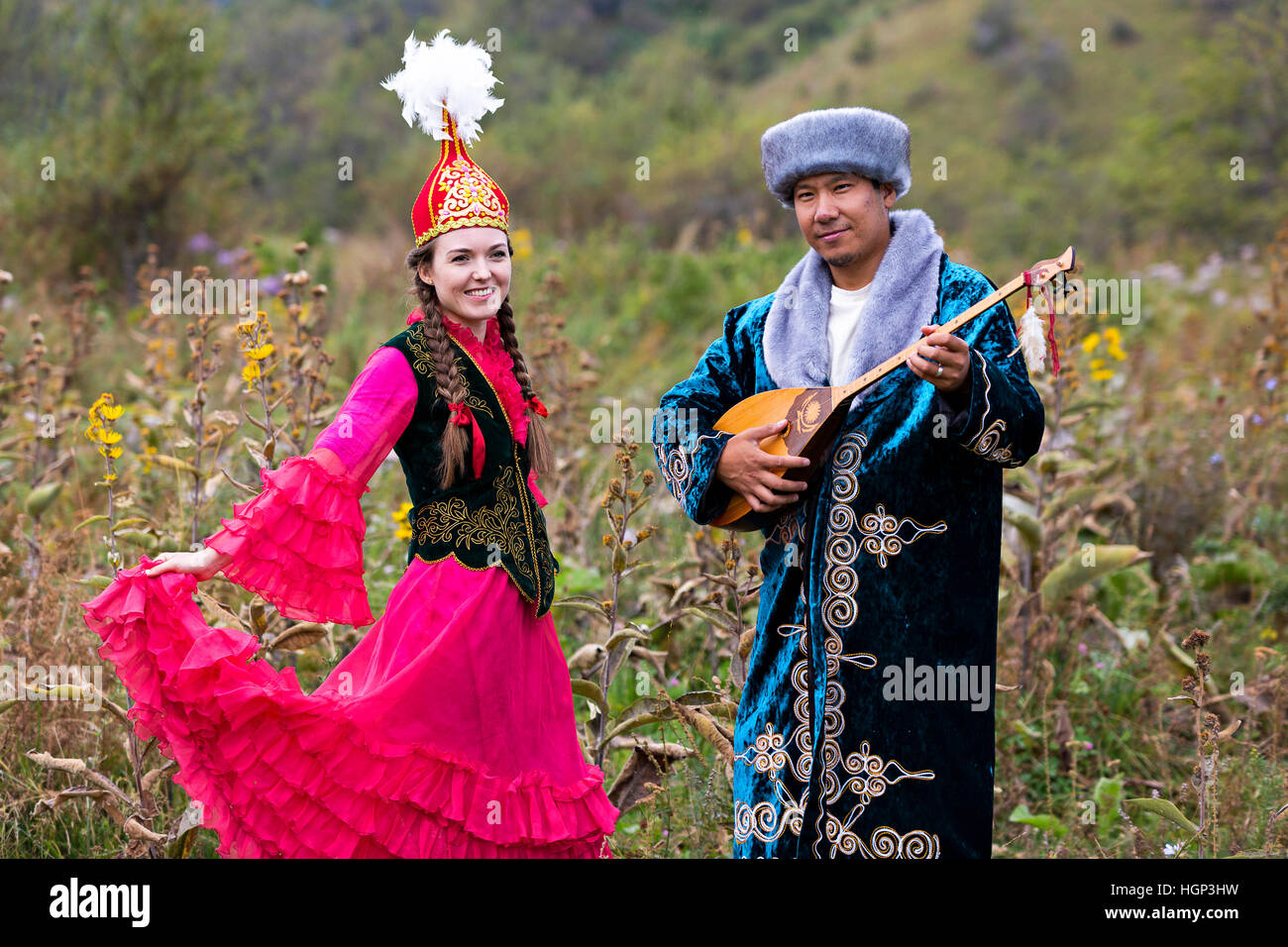 Kazakh homme jouant l'instrument de musique national de dombra et de femme dans des danses rouges à Almaty, Kazakhstan Banque D'Images