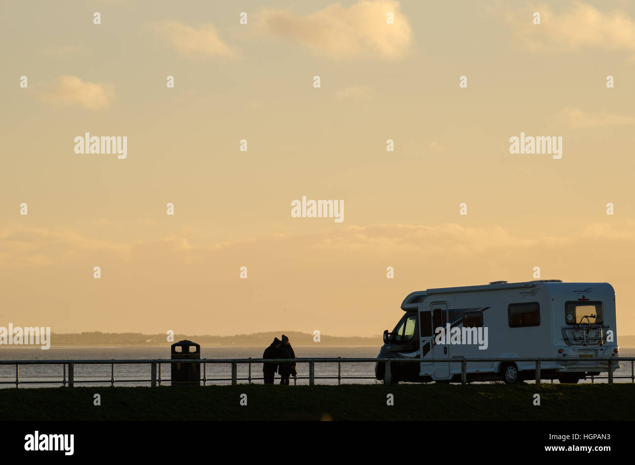 Un couple s'ouvrent sur l'estuaire de Ribble, à côté d'une autocaravane au coucher du soleil Banque D'Images
