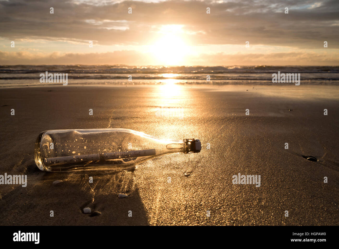 Message dans une bouteille échouée sur la plage au coucher du soleil Banque D'Images