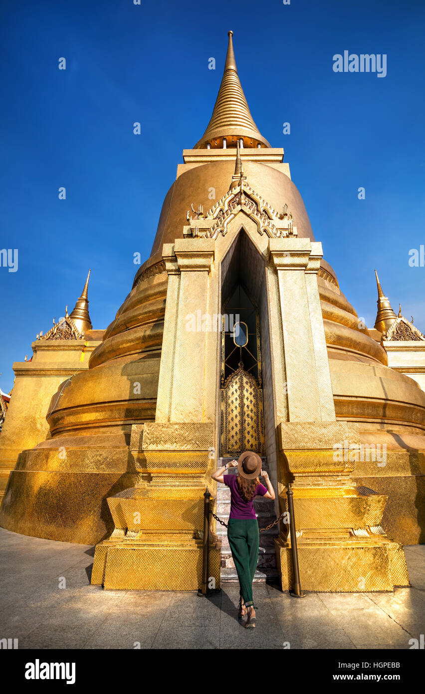 Touriste marche dans le Temple du Bouddha d'Émeraude près de grand stupa doré à Bangkok au coucher du soleil Banque D'Images