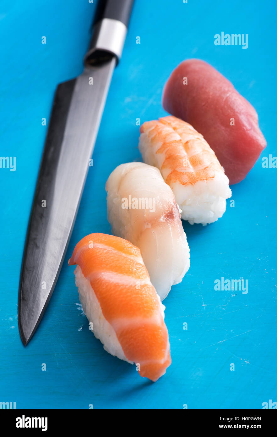 Quatre différents nighiri sushi avec des tranches de matières premières, frais, Saumon, Loup de mer, le crabe et le thon sur les monticules de riz avec un long couteau chefs, high angle vie Banque D'Images