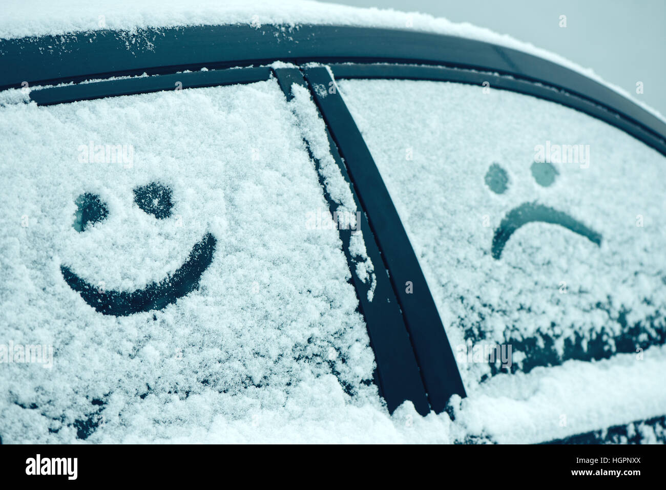 Heureux et triste émoticône smiley face dans la neige sur les vitres des voitures, saison hiver joie et bonheur concept Banque D'Images