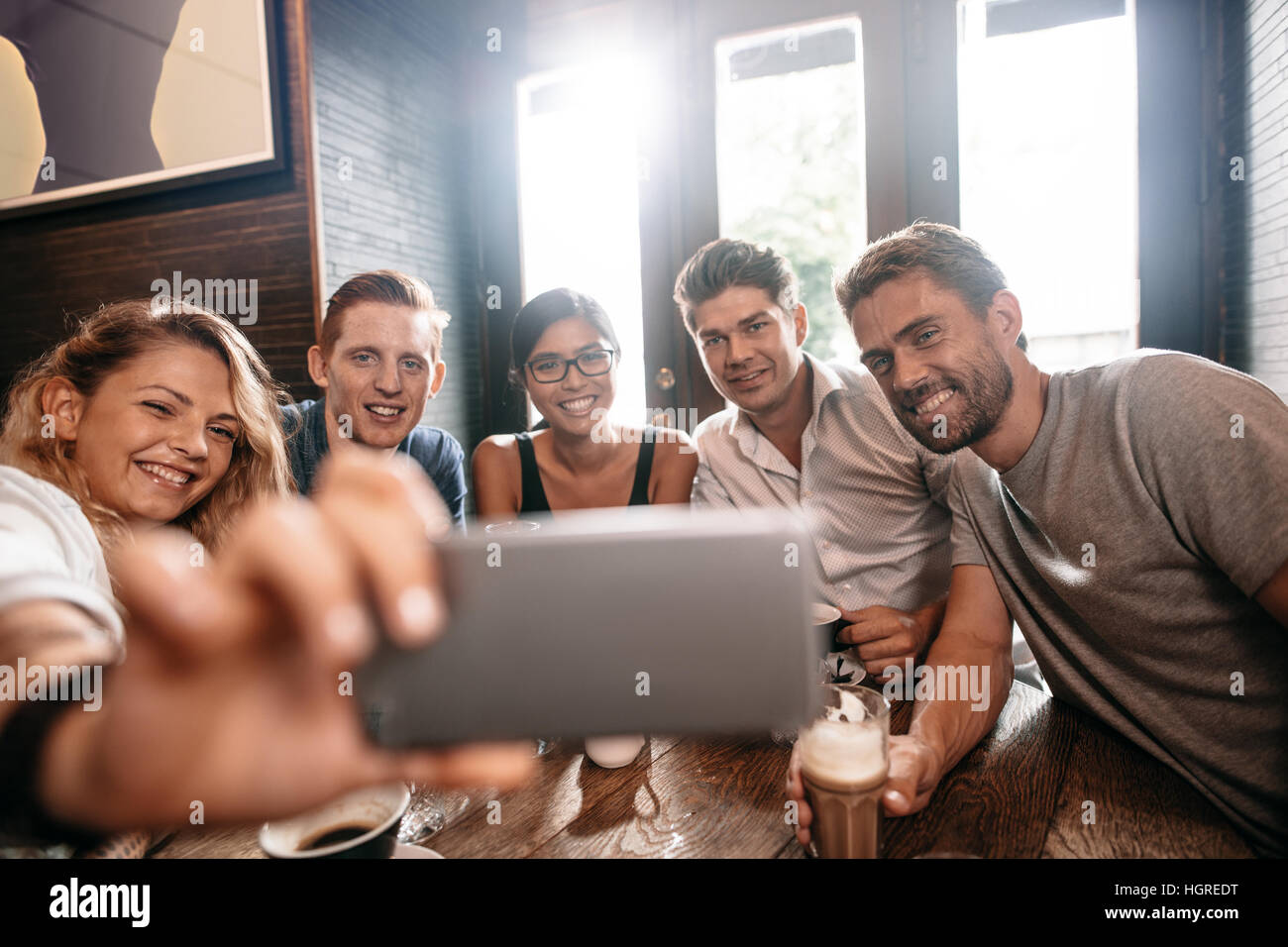 Divers groupes d'amis en tenant sur selfies téléphone intelligent. Les jeunes, hommes et femmes, assis à table et de prendre un café self portrait sur téléphone cellulaire. Banque D'Images