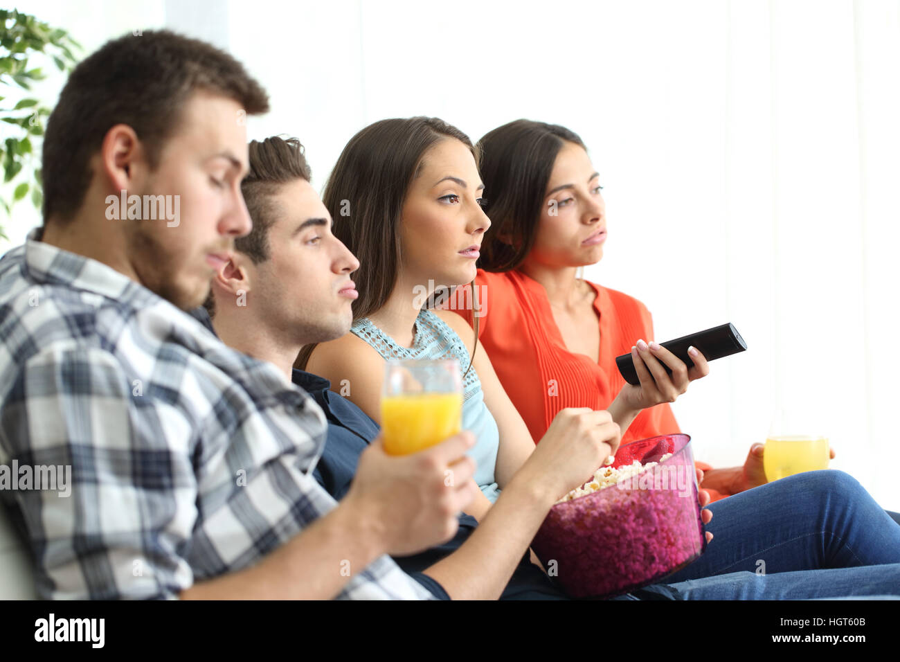 Vue latérale d'ennuyer groupe de quatre amis de regarder un mauvais programme tv assis sur un canapé dans le salon d'un appartement Banque D'Images