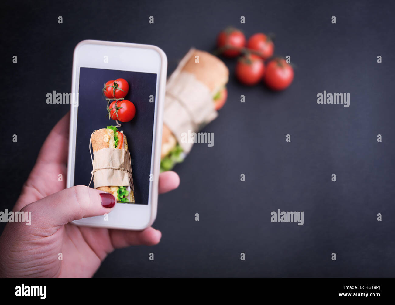 Main humaine avec les téléphones intelligents pour prendre des photos de sandwich sur fond noir. La photographie alimentaire téléphone mobile Banque D'Images