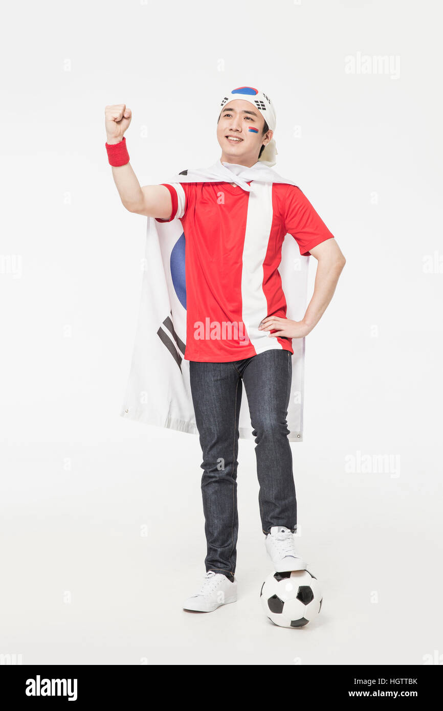 Young smiling Korean cheerleader homme marchant sur un ballon de foot Banque D'Images